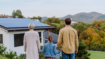 PV-Versicherung. Familie steht vor Einfamilienhaus mit PV-Anlage.