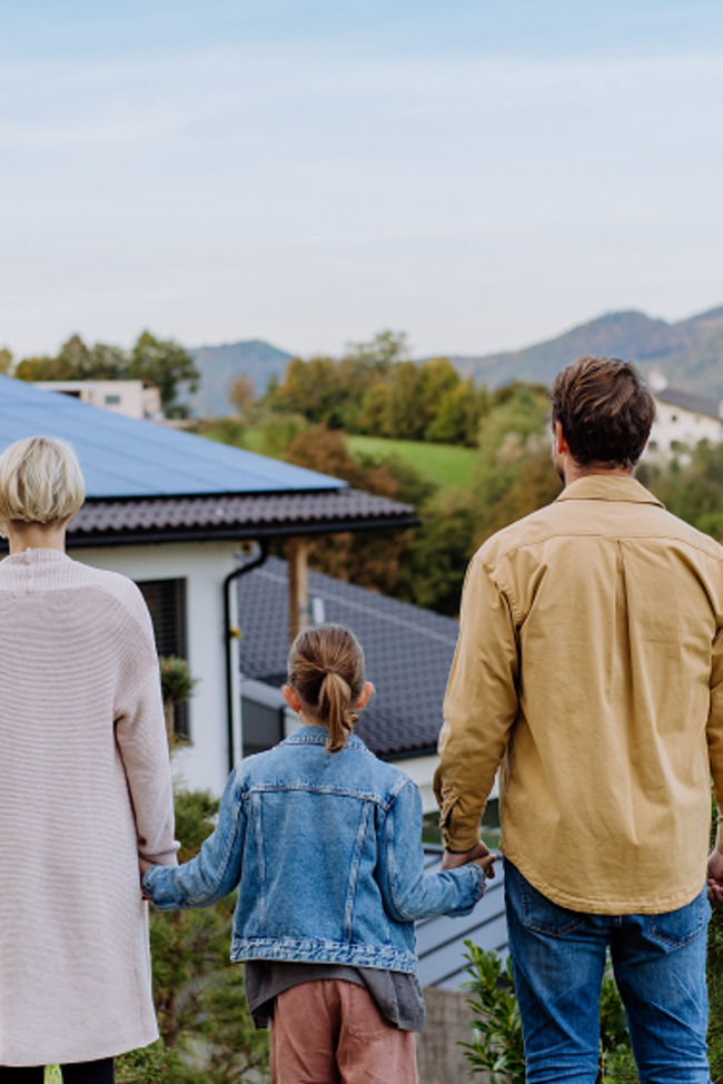 PV-Versicherung. Familie steht vor Einfamilienhaus mit PV-Anlage. 