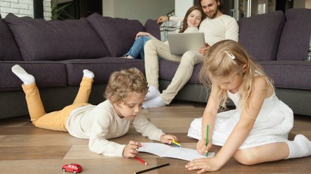 Paar sitzt auf Couch während Kinder am Boden sitzen und Malen.