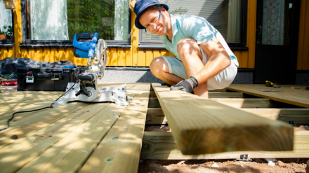 Mann baut Holzterrasse vor seinem Tiny House und schaut dabei in die Kamerla