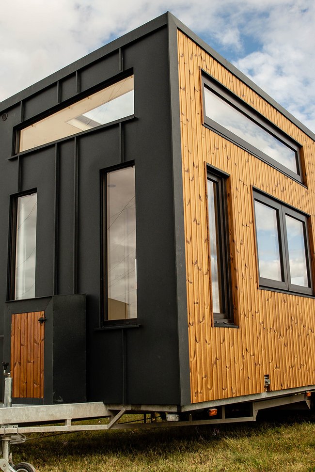 Tiny Haus auf Wiese mit Anhängerkupplung.