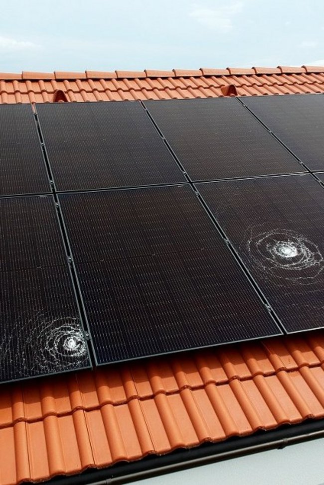 Symbolbild zeigt Hagelschäden auf einer am Dach montierten PV-Anlage