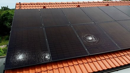 Symbolbild zeigt Hagelschäden auf einer am Dach montierten PV-Anlage