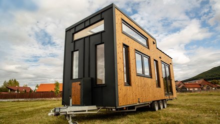 Symbolbild Tiny House zeigt Tiny House auf Anhänger, welcher auf einer Wiese steht.