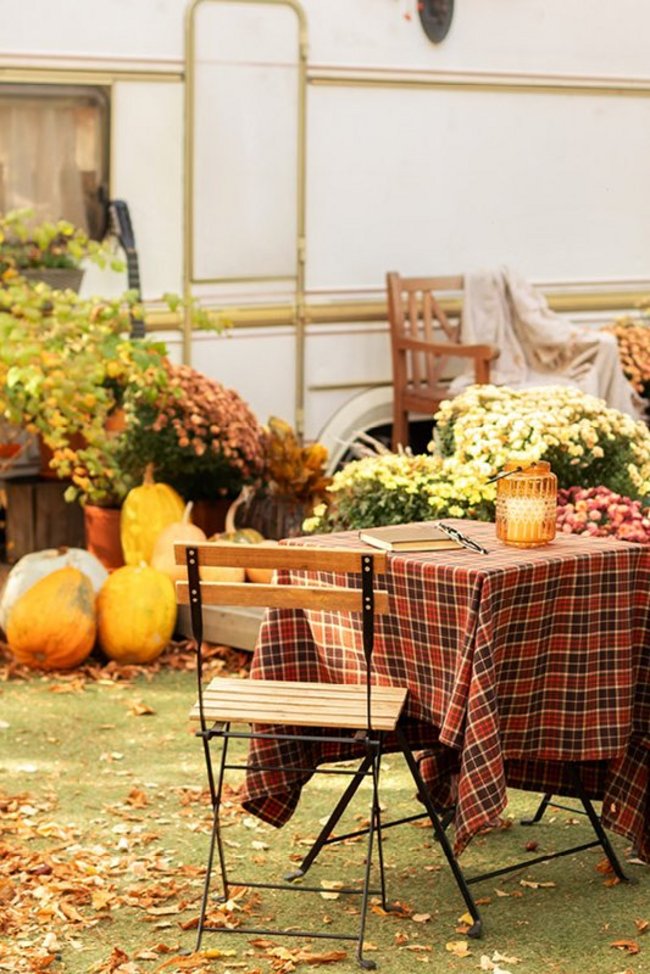 Herbstlich dekorierter Gartentisch mit Stühlen vor einem Wohnwagen.