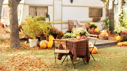 Herbstlich dekorierter Gartentisch mit Stühlen vor einem Wohnwagen.