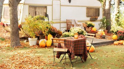 Dauercamperversicherung Herbstlich dekorierter Gartentisch mit Stühlen vor einem Wohnwagen.