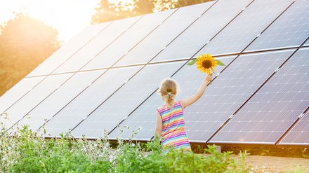 Kleines Mädchen mit Sonnenblume vor PV-Anlage
