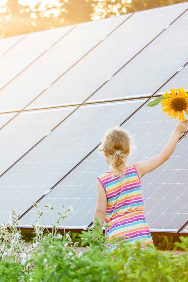 Kleines Mädchen mit Sonnenblume vor PV-Anlage
