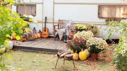 Herbstlich dekorierter Gartentisch mit Stühlen vor einem Wohnwagen.