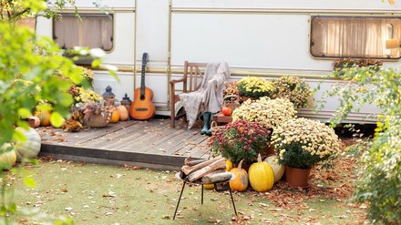 2505461139 Herbstlich dekorierter Gartentisch mit Stühlen vor einem Wohnwagen.